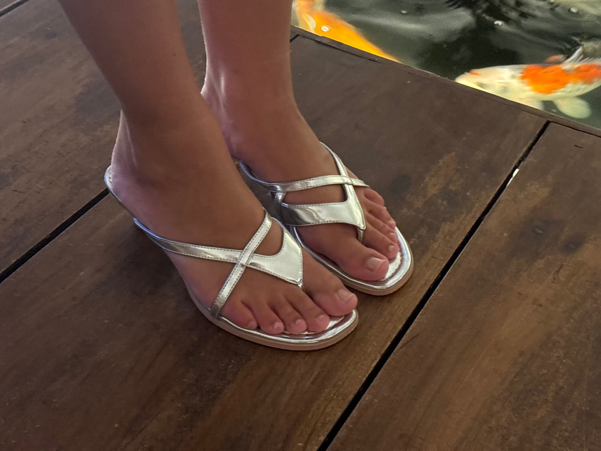 Silver kitten heel sandals worn on a wooden deck
